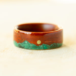 Wooden ring with green inlay and gold dot on a light background