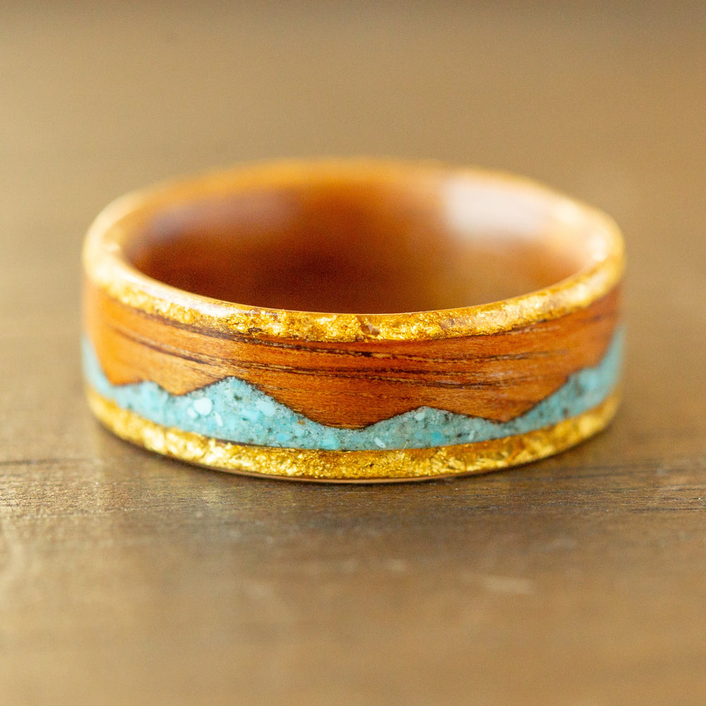 Wooden ring with gold and turquoise inlay on a wooden surface