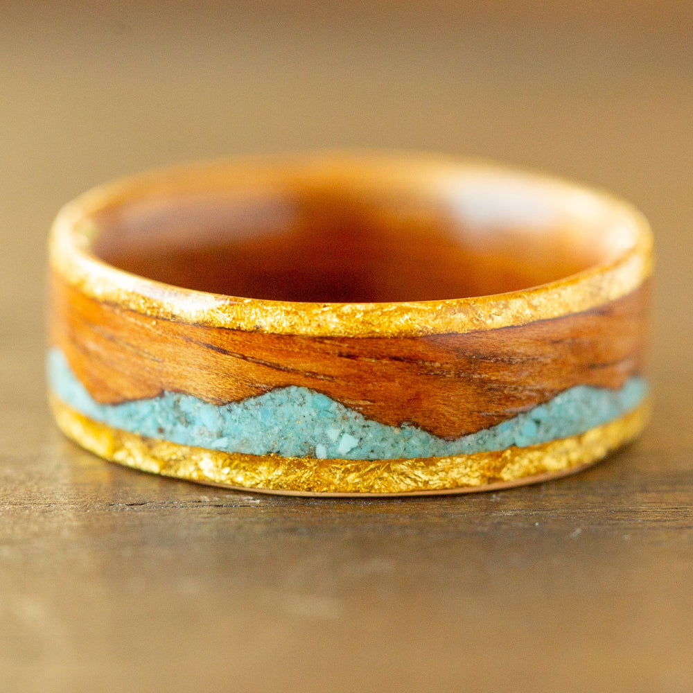 Wooden ring with gold and turquoise inlay on a wooden surface