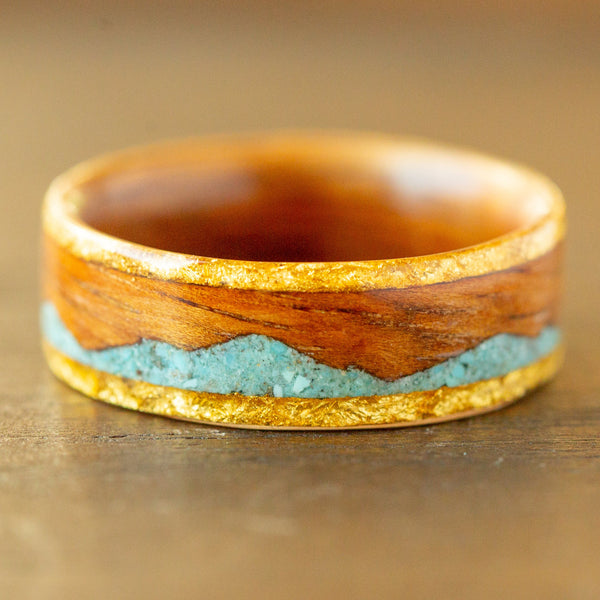 Wooden ring with gold and turquoise inlay on a wooden surface